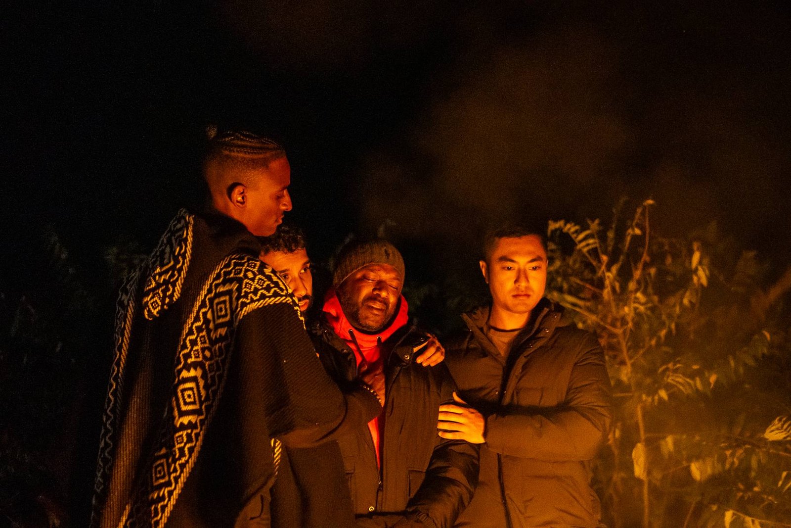 Men holding one another around a night fire