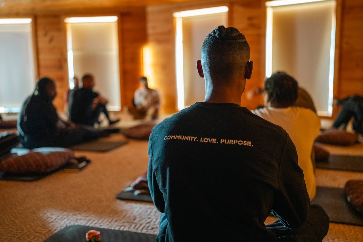 Men seated in a circle on cushions, one wearing a Community Love Purpose shirt